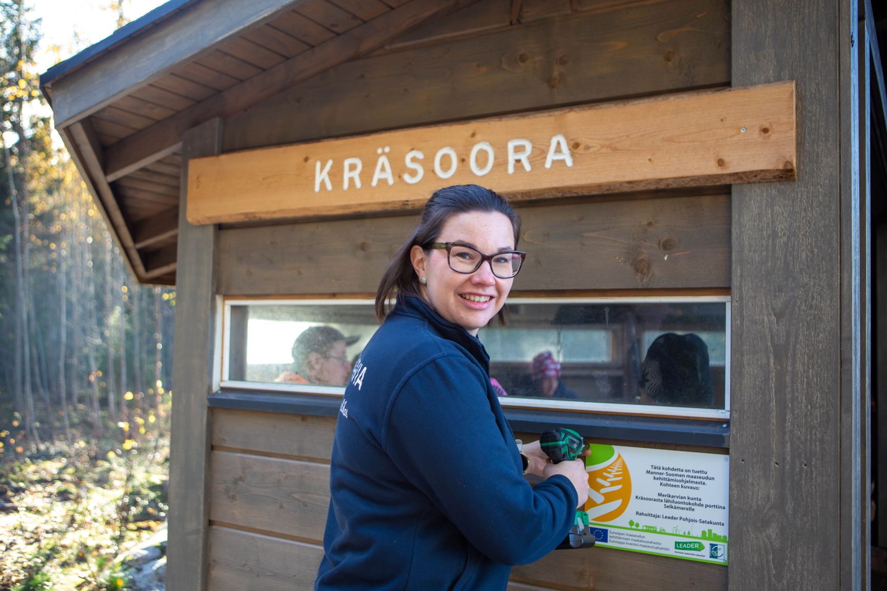 Noora-Mari Iisakkala kiinnittää maaseuturahoituksen kylttiä laavuun.