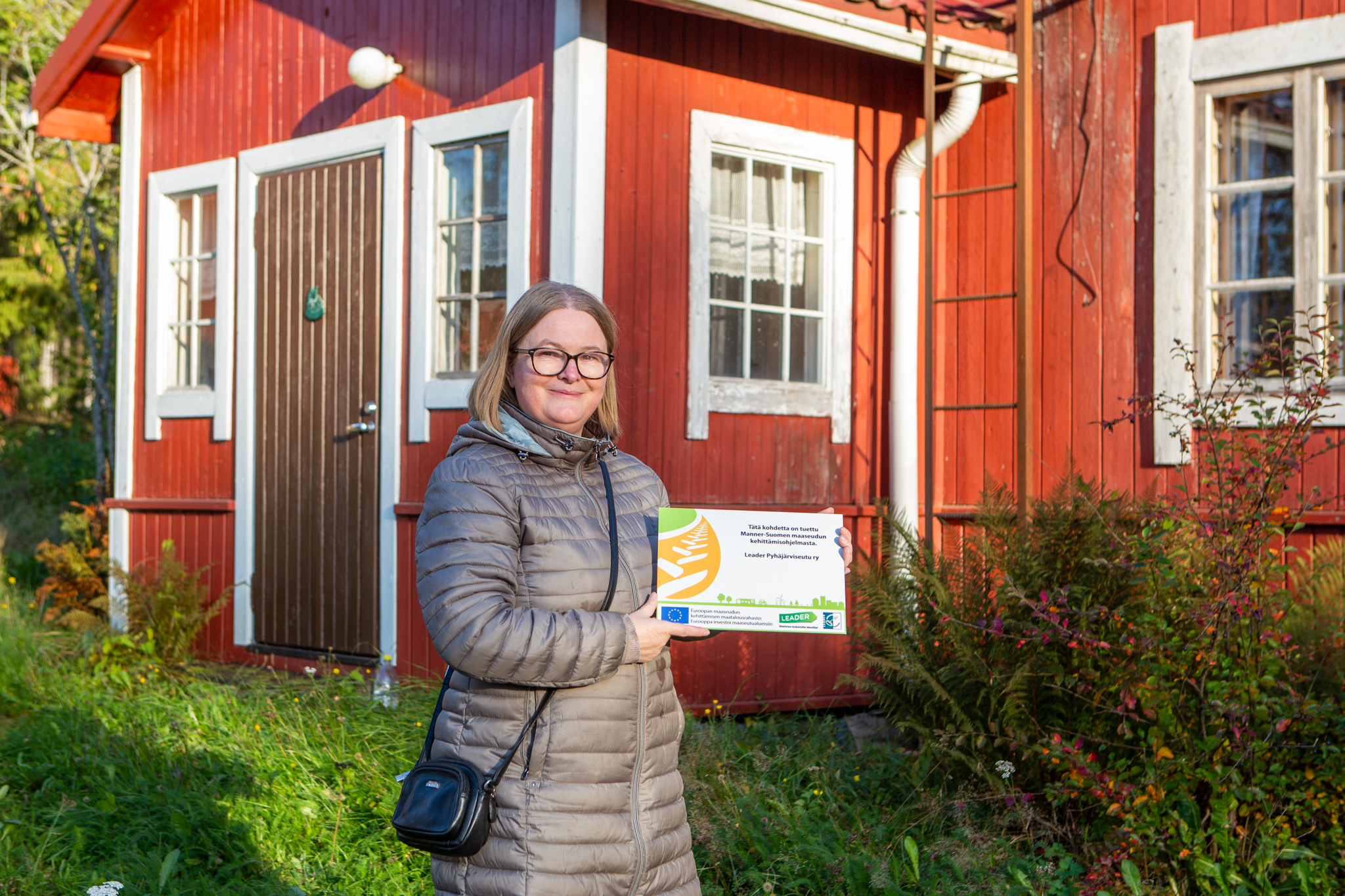 Sanna Kinnunen näyttää maaseuturahoituksen kylttiä Tuiskulan kulttuurikeskuksella