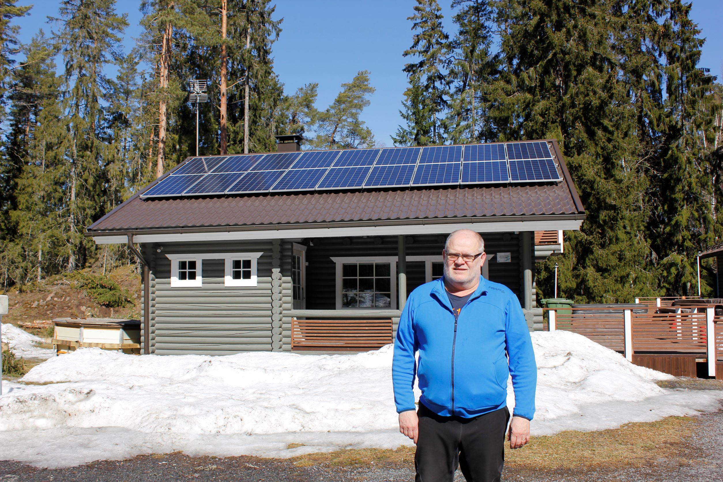 Leirikosken mökki taustalla aurinkopaneelit katolla henkilö sinisessä paidassa etualalla